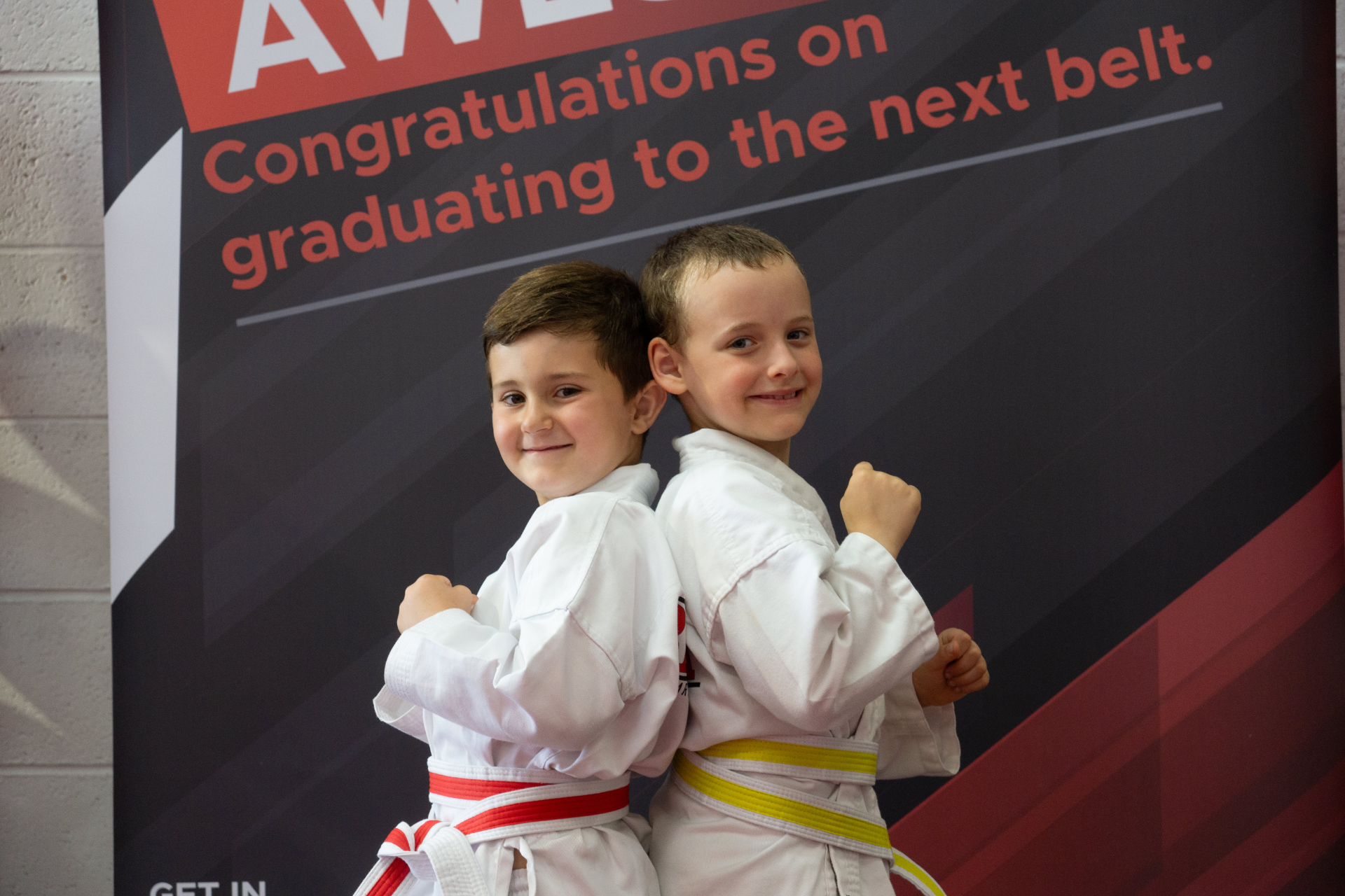 Two young Benefit Martial Arts students in front of a belt grading banner